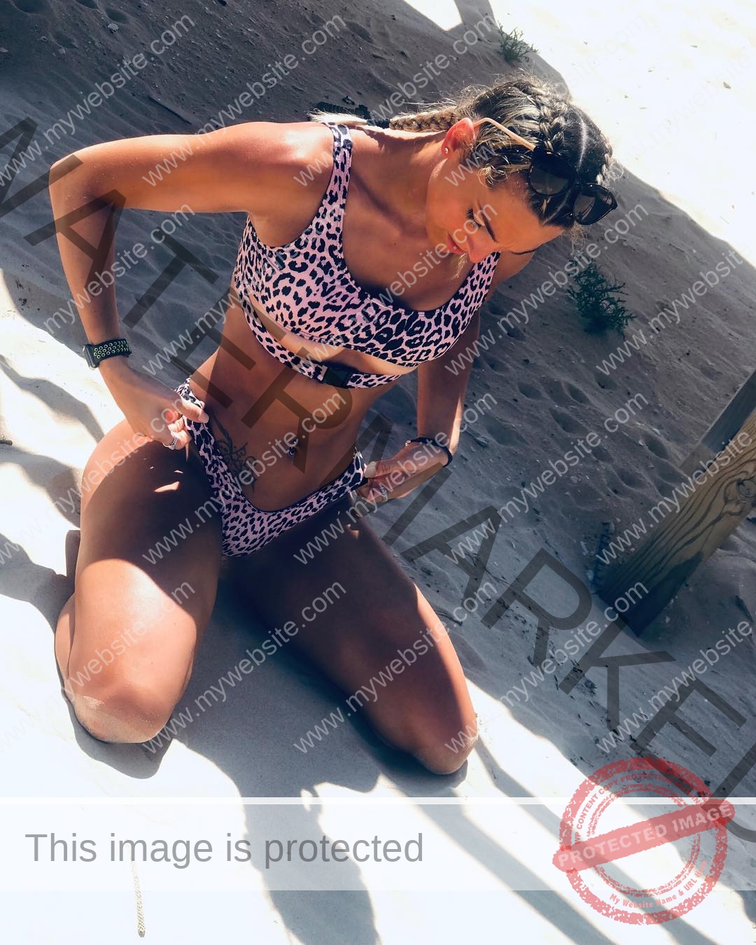 charlotte-wingfield-malta-charlottewingfield.oly-04134 Charlotte Wingfield, track athlete from Malta, kneels on sand, adjusts her pink and black leopard bikini, sunlight casting shadows.