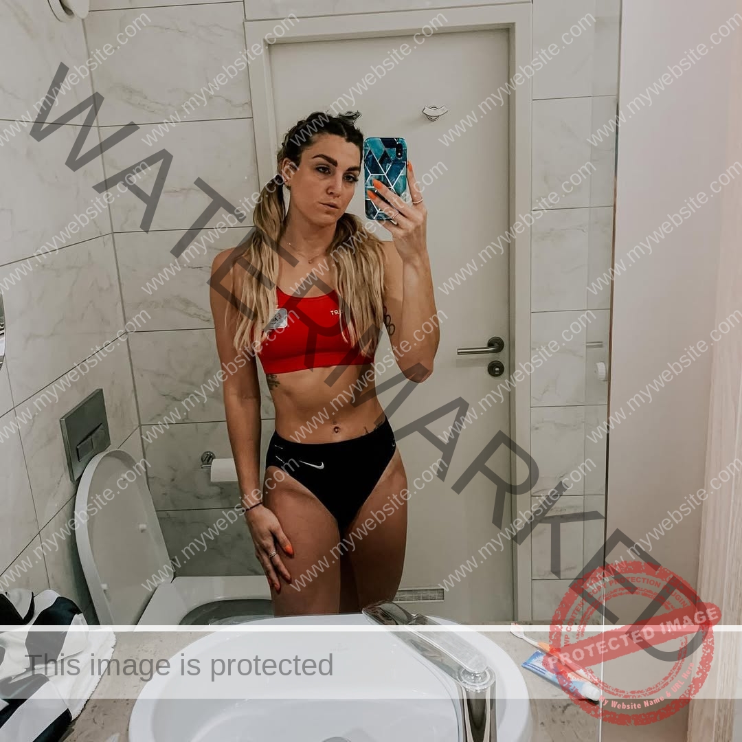 charlotte-wingfield-malta-charlottewingfield.oly-04271 Charlotte Wingfield, track athlete from Malta, wears a red sports bra and black bottoms taking a selfie in a tiled bathroom with toiletries.