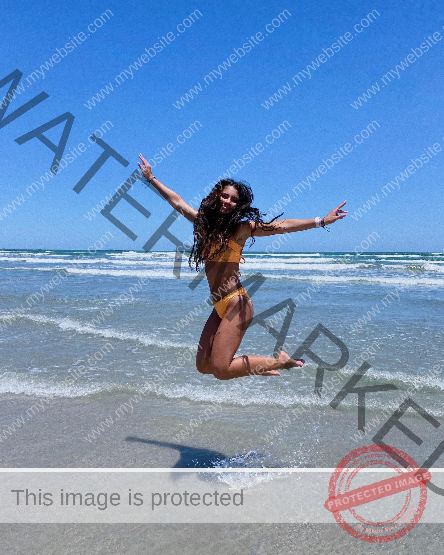 ciandra-carrico-trinity-ciandracarrico-3973 Ciandra Carrico, track athlete from Trinity, in a yellow bikini jumps joyfully on a sunny beach with waves and blue sky behind.