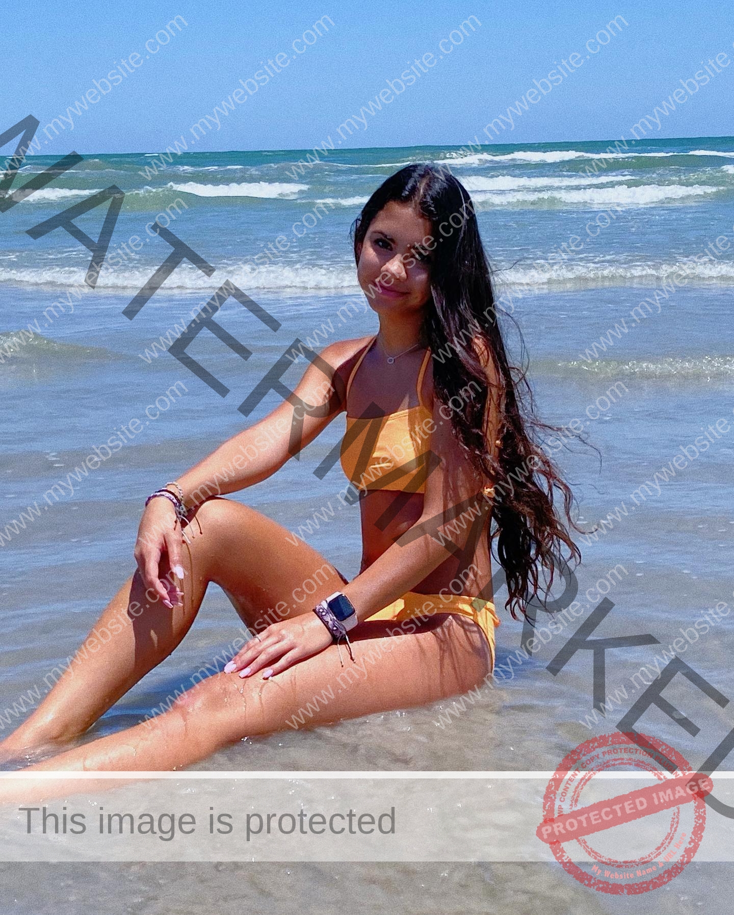 ciandra-carrico-trinity-ciandracarrico-3978 Ciandra Carrico, track athlete from Trinity, in a yellow bikini sits smiling in shallow ocean water as waves roll in under a clear sky.