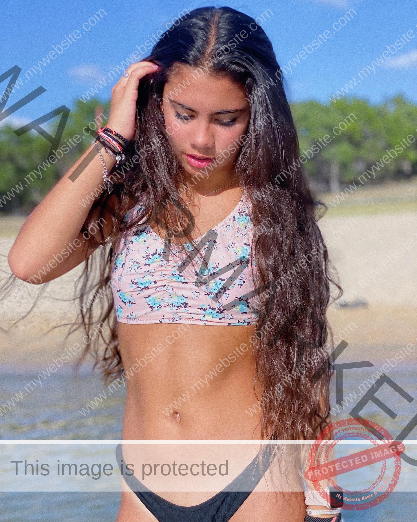 ciandra-carrico-trinity-ciandracarrico-3989 Ciandra Carrico, track athlete from Trinity, stands by the beach in a floral crop top and black bikini bottoms, looking down.