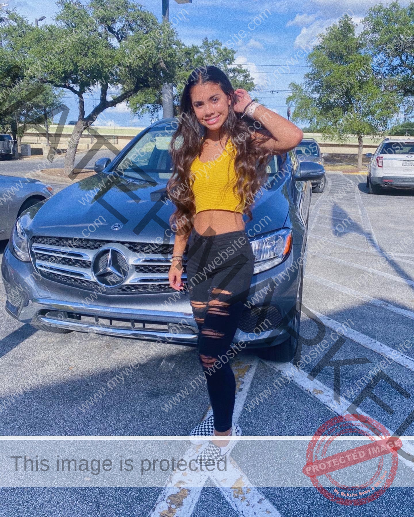 ciandra-carrico-trinity-ciandracarrico-3990 Ciandra Carrico, track athlete from Trinity, with long wavy hair in a yellow crop top stands by a silver Mercedes-Benz in the sun.