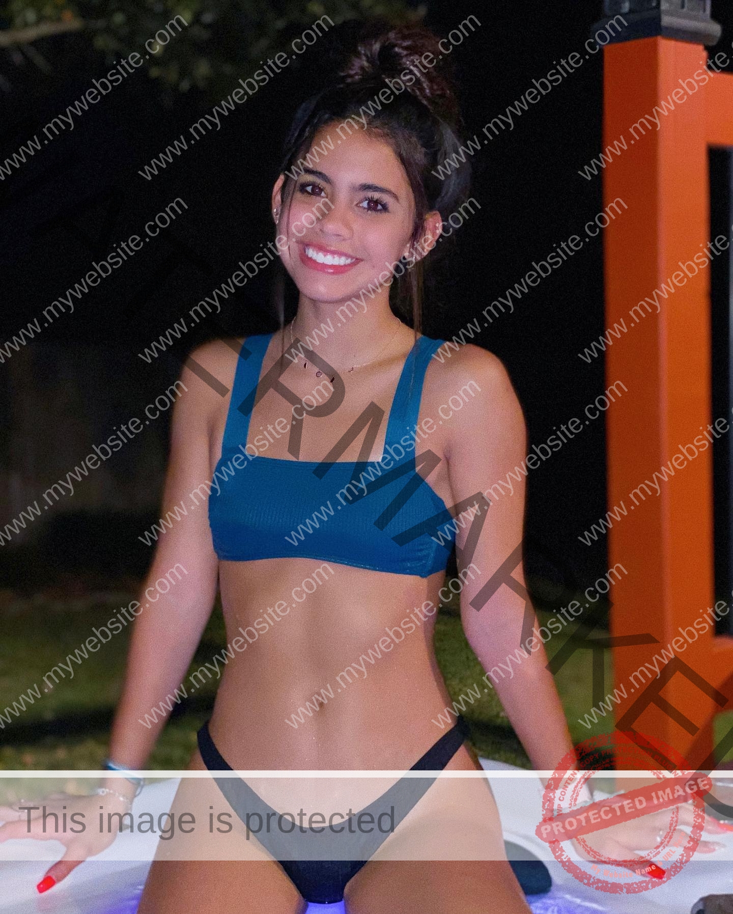 ciandra-carrico-trinity-ciandracarrico-4006 Ciandra Carrico, track athlete from Trinity, with dark hair in a bun, wears a blue bikini top and black bottoms by an outdoor hot tub at night.