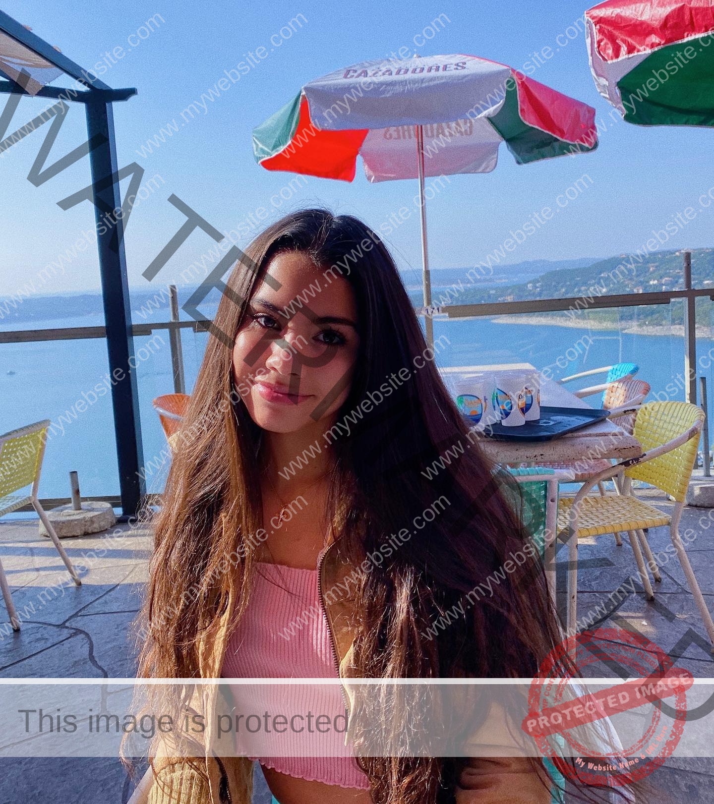 ciandra-carrico-trinity-ciandracarrico-4015 Ciandra Carrico, track athlete from Trinity, with long brown hair at an outdoor café by a scenic blue lake with hills and umbrellas.