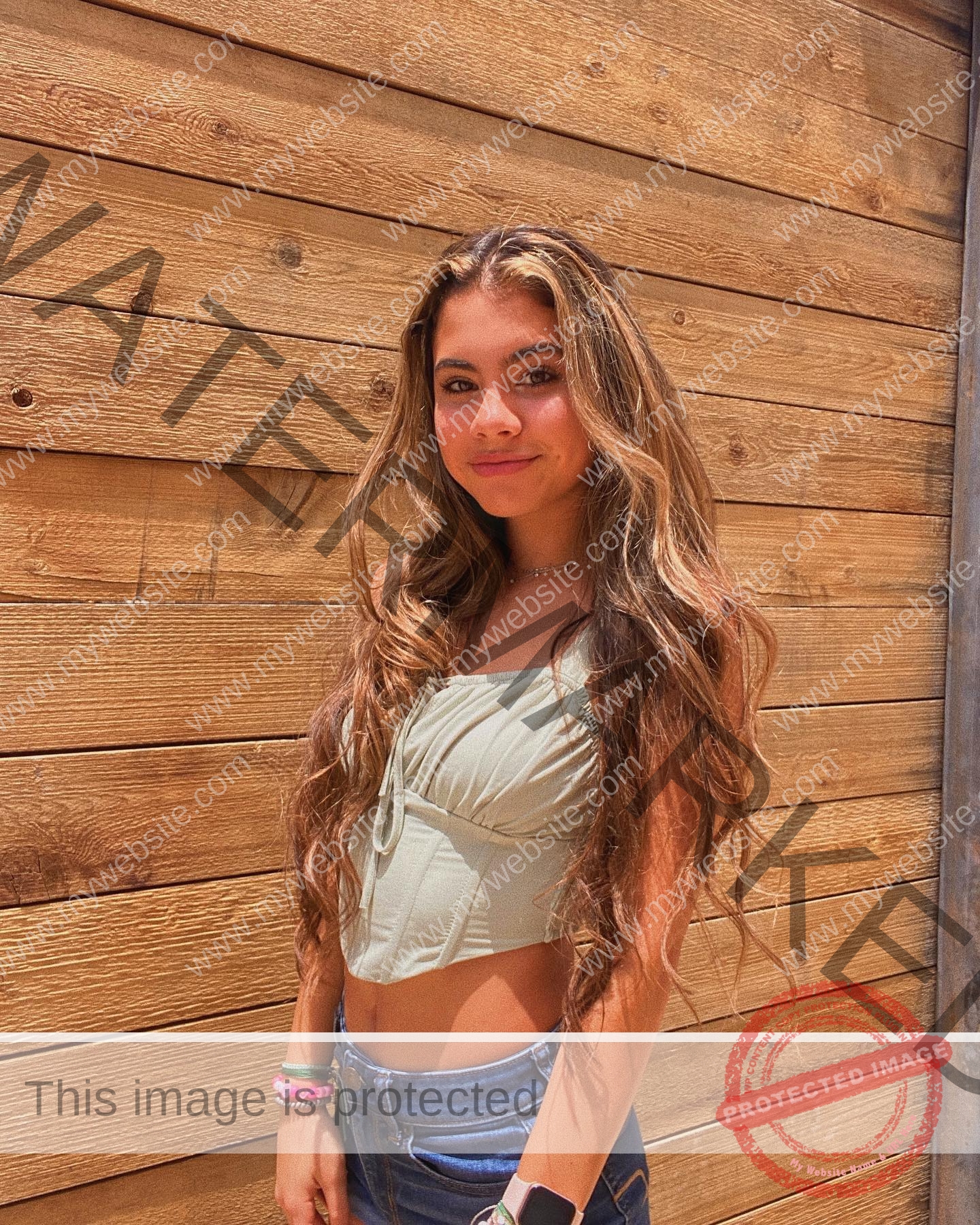ciandra-carrico-trinity-ciandracarrico-4051 Ciandra Carrico, track athlete from Trinity, stands before a wooden wall in a green crop top and jeans, sunlight on her smiling face.