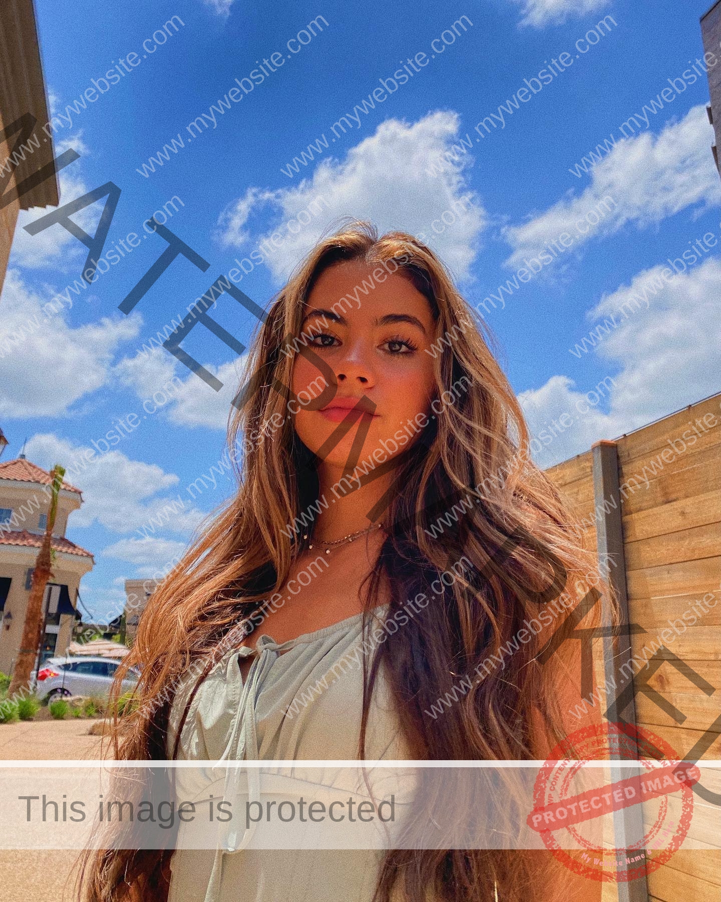 ciandra-carrico-trinity-ciandracarrico-4054 Ciandra Carrico, track athlete from Trinity, with long brown hair and a blue dress stands outdoors under a bright blue sky.