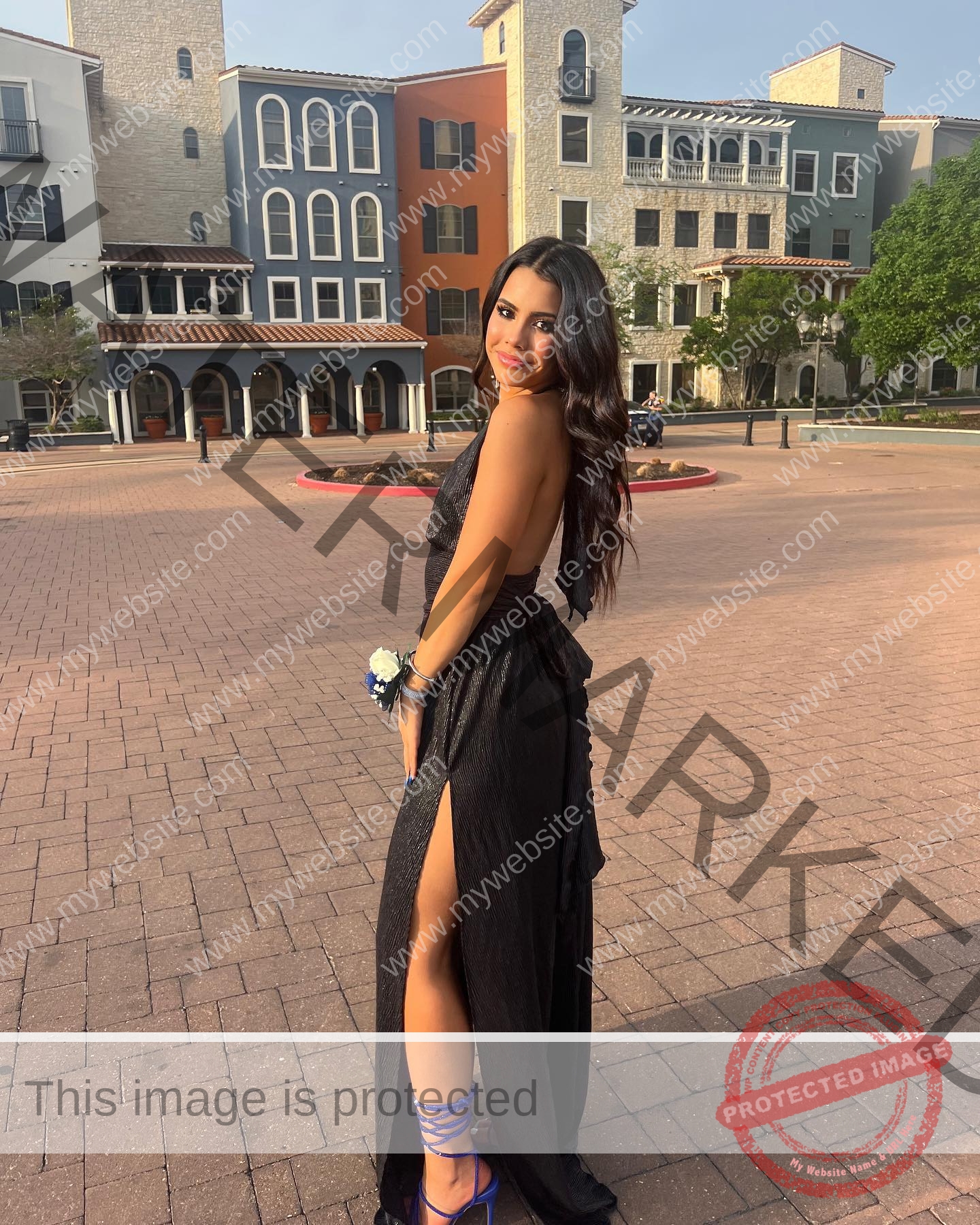 ciandra-carrico-trinity-ciandracarrico-4207 Ciandra Carrico, track athlete from Trinity, in a black gown with high slit, blue heels, corsage; smiling on plaza, buildings behind.