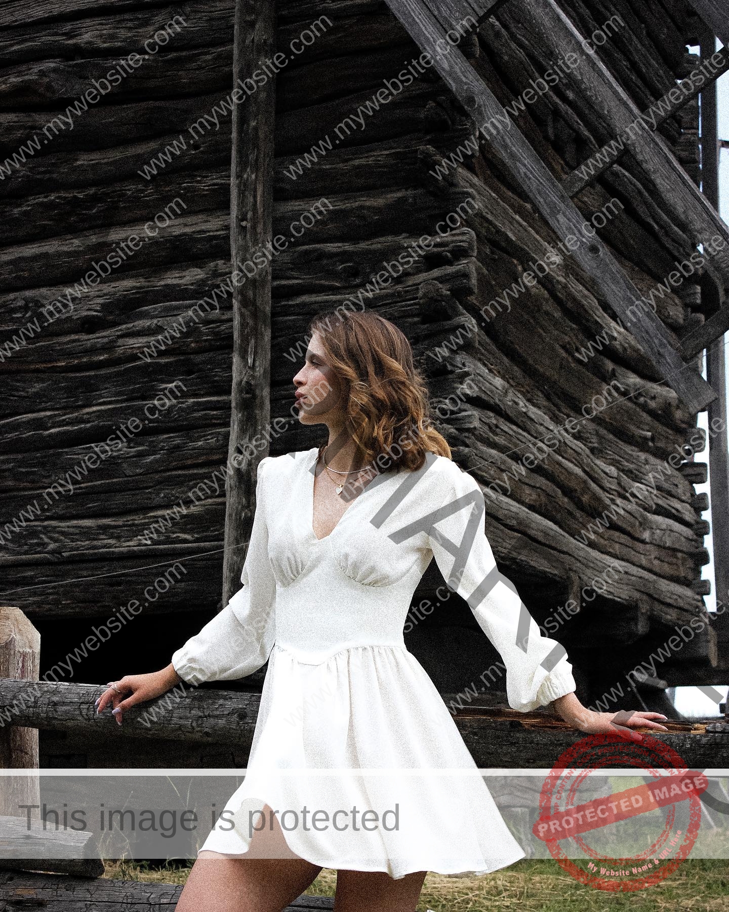 daria-polyanskaya-ukraine-polyanska.ya-x-08534 Daria-Polyanskaya, track athlete from Ukraine, stands outdoors in a white dress by a rustic wooden building with logs and green grass.