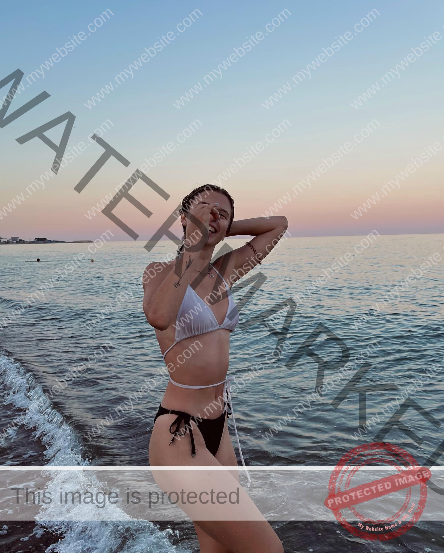 daria-polyanskaya-ukraine-polyanska.ya-x-08539 Daria-Polyanskaya, track athlete from Ukraine stands at the sea in a bikini at sunset, posing with one hand on her head.