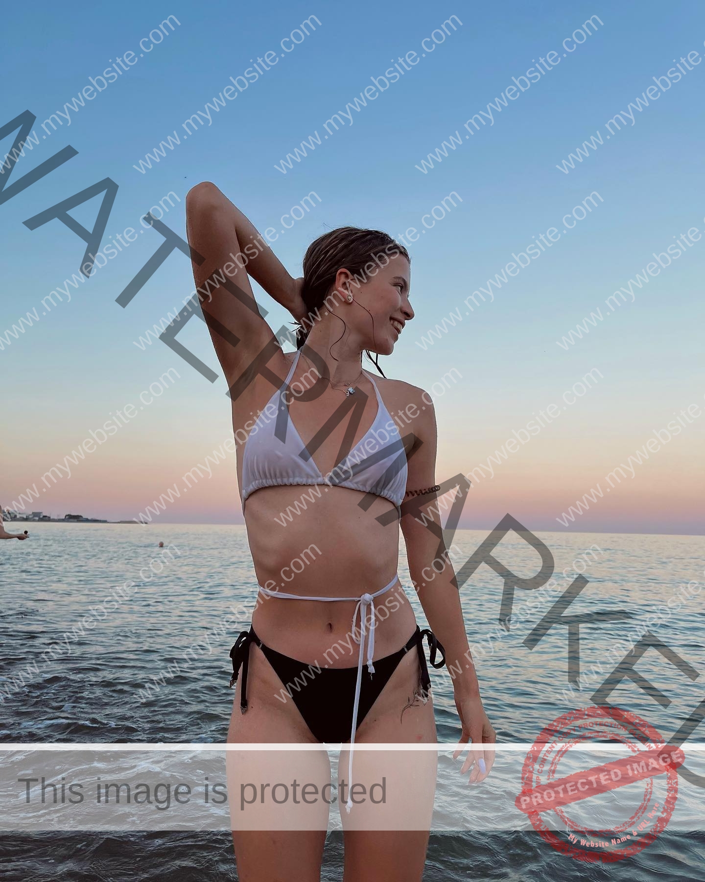 daria-polyanskaya-ukraine-polyanska.ya-x-08541 Daria-Polyanskaya, track athlete from Ukraine, stands in shallow sea at sunset in a bikini, looking aside with an arm behind her head.