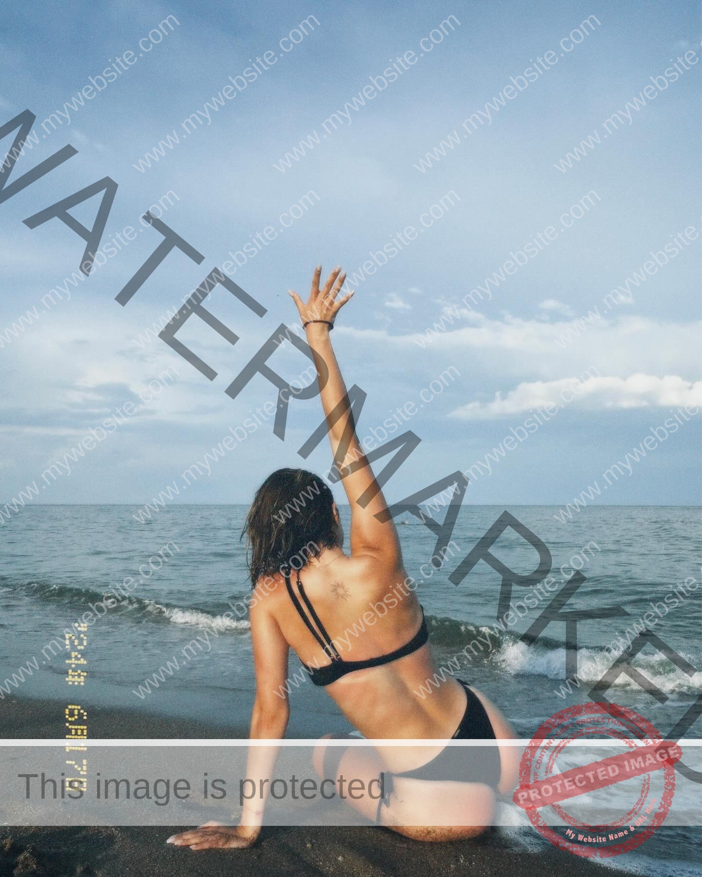 daria-polyanskaya-ukraine-polyanska.ya-x-08591 Daria-Polyanskaya, track athlete from Ukraine sits in a black bikini on sandy shore, one arm raised, waves and clouds behind.