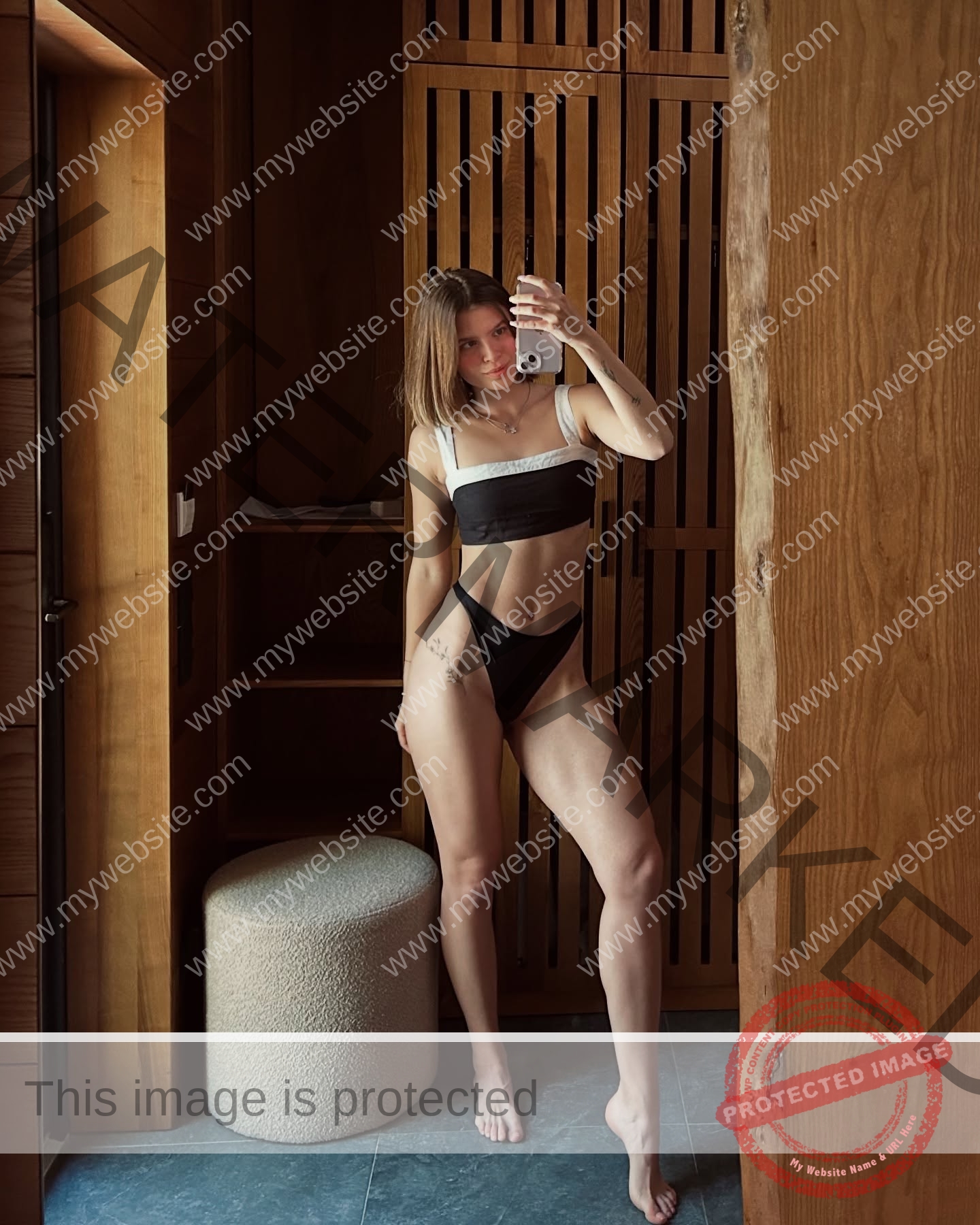 daria-polyanskaya-ukraine-polyanska.ya-x-08676 Daria-Polyanskaya, track athlete from Ukraine, stands barefoot in a two-piece swimsuit taking a mirror selfie in a wood-paneled room.