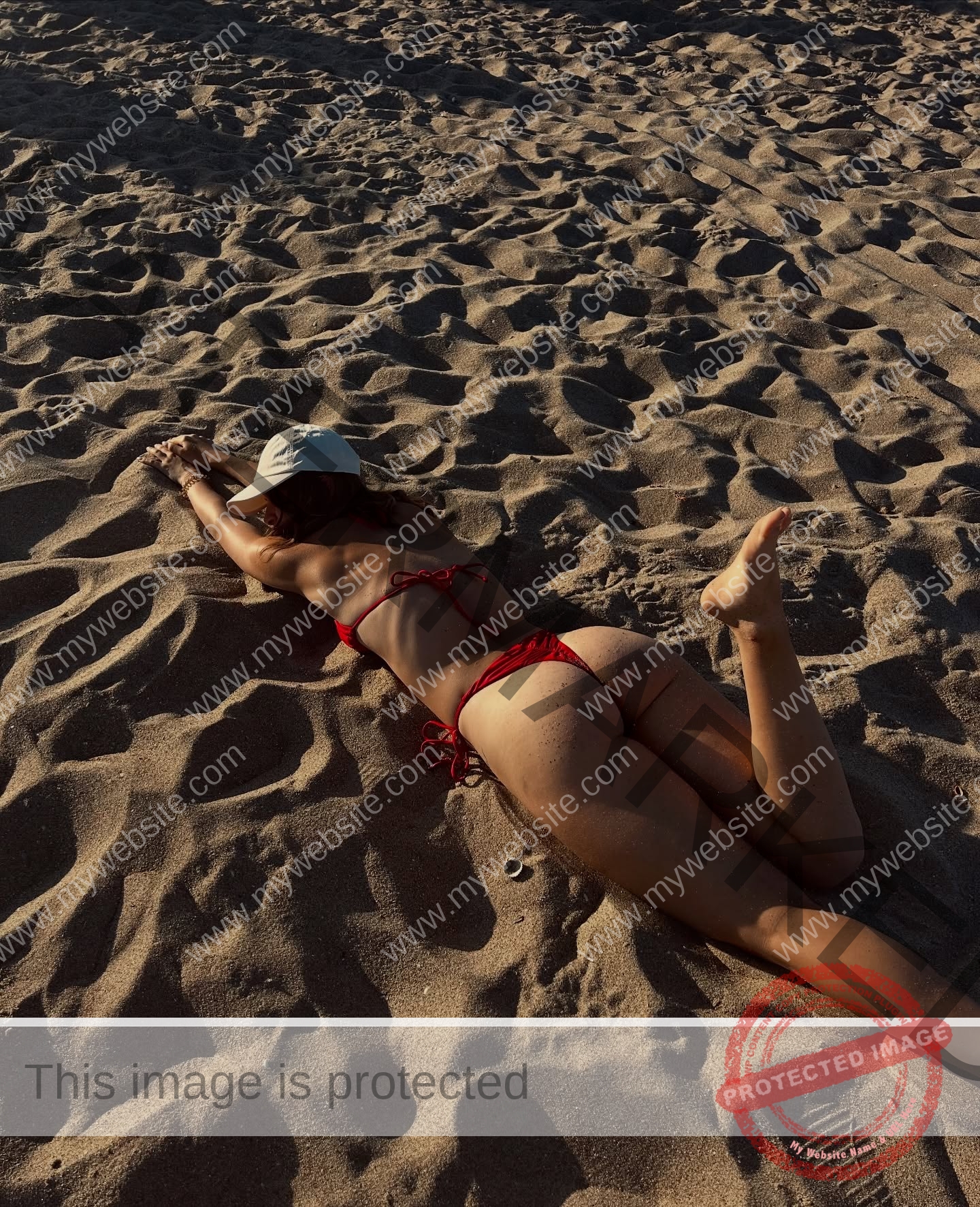 daria-polyanskaya-ukraine-polyanska.ya-x-08735 Daria-Polyanskaya, track athlete from Ukraine, in a red bikini and white cap lies face down on sunlit sand, arms stretched forward.