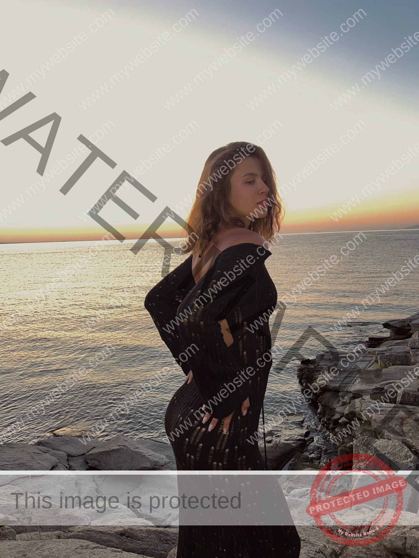 daria-polyanskaya-ukraine-polyanska.ya-x-08767 Daria-Polyanskaya, track athlete from Ukraine in a sheer black dress stands on rocky shore at sunset, gazing over her shoulder.