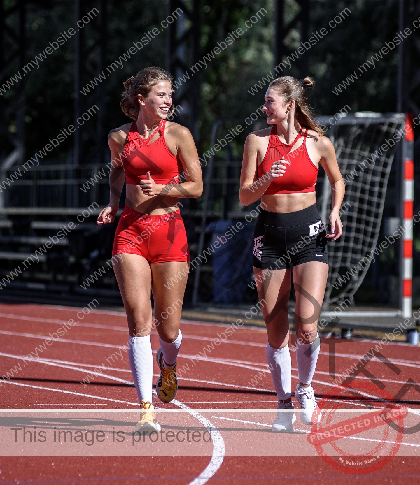 daria-polyanskaya-ukraine-polyanska.ya-x-08791 Daria-Polyanskaya, track athlete from Ukraine 'Two young women in athletic wear jogging and smiling on a red running track with bleachers.'.