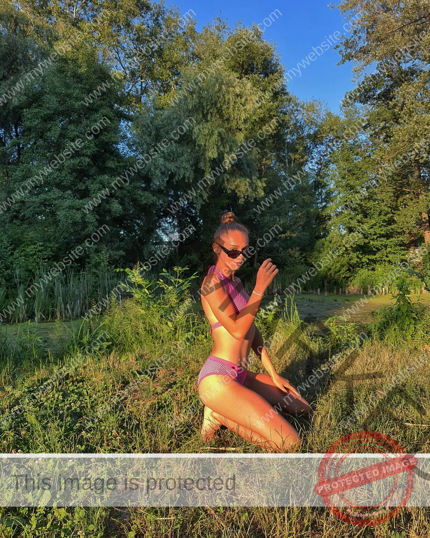 diana-honcharenka-ukraine-goncharenko_43-09523 Diana Honcharenka, track athlete from Ukraine, in a pink bikini and sunglasses kneels on grass amid sunlit trees, late afternoon.