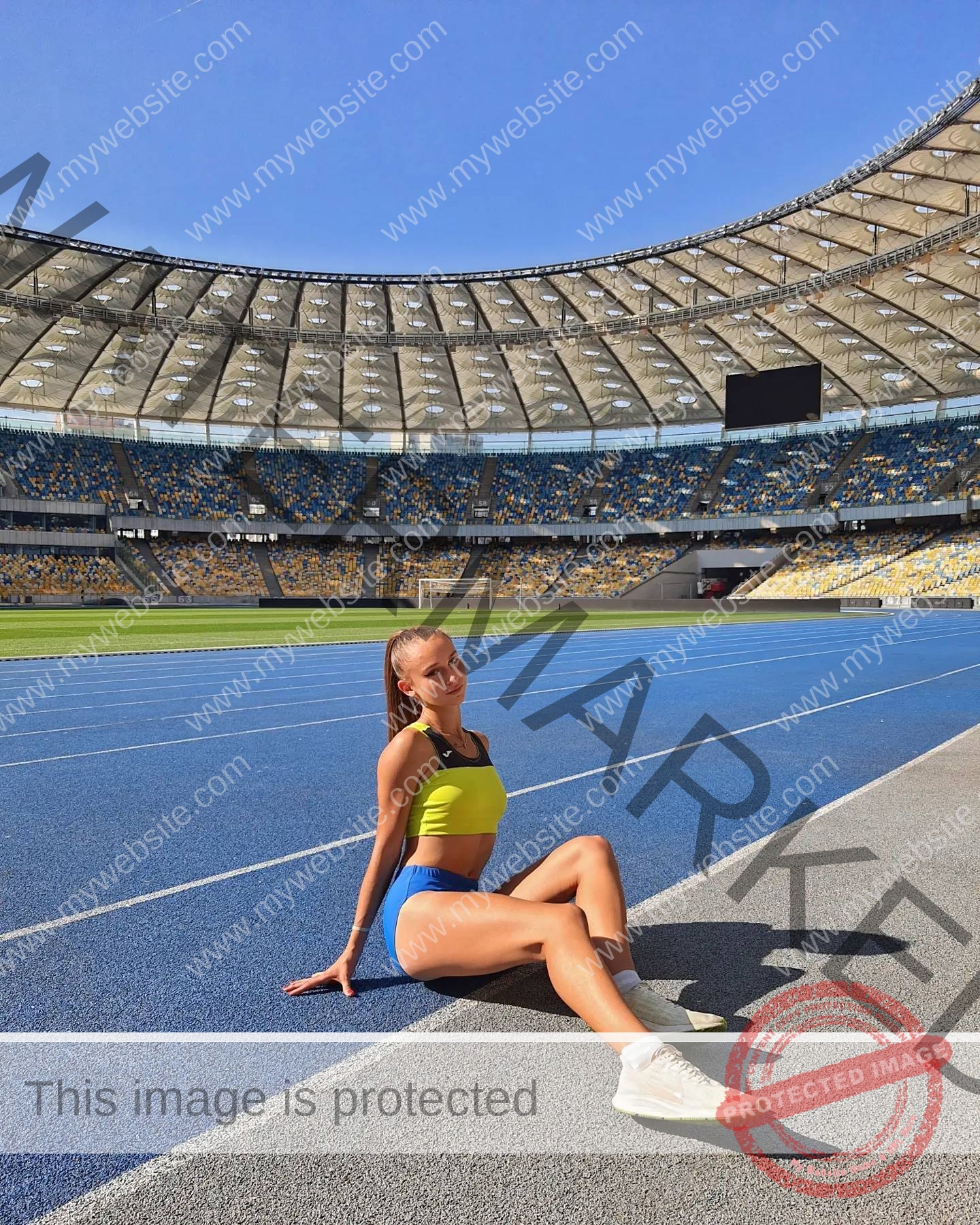 diana-honcharenka-ukraine-goncharenko_43-09555 Diana Honcharenka, track athlete from Ukraine, sits in athletic wear on a blue running track in a sunny, mostly empty stadium.