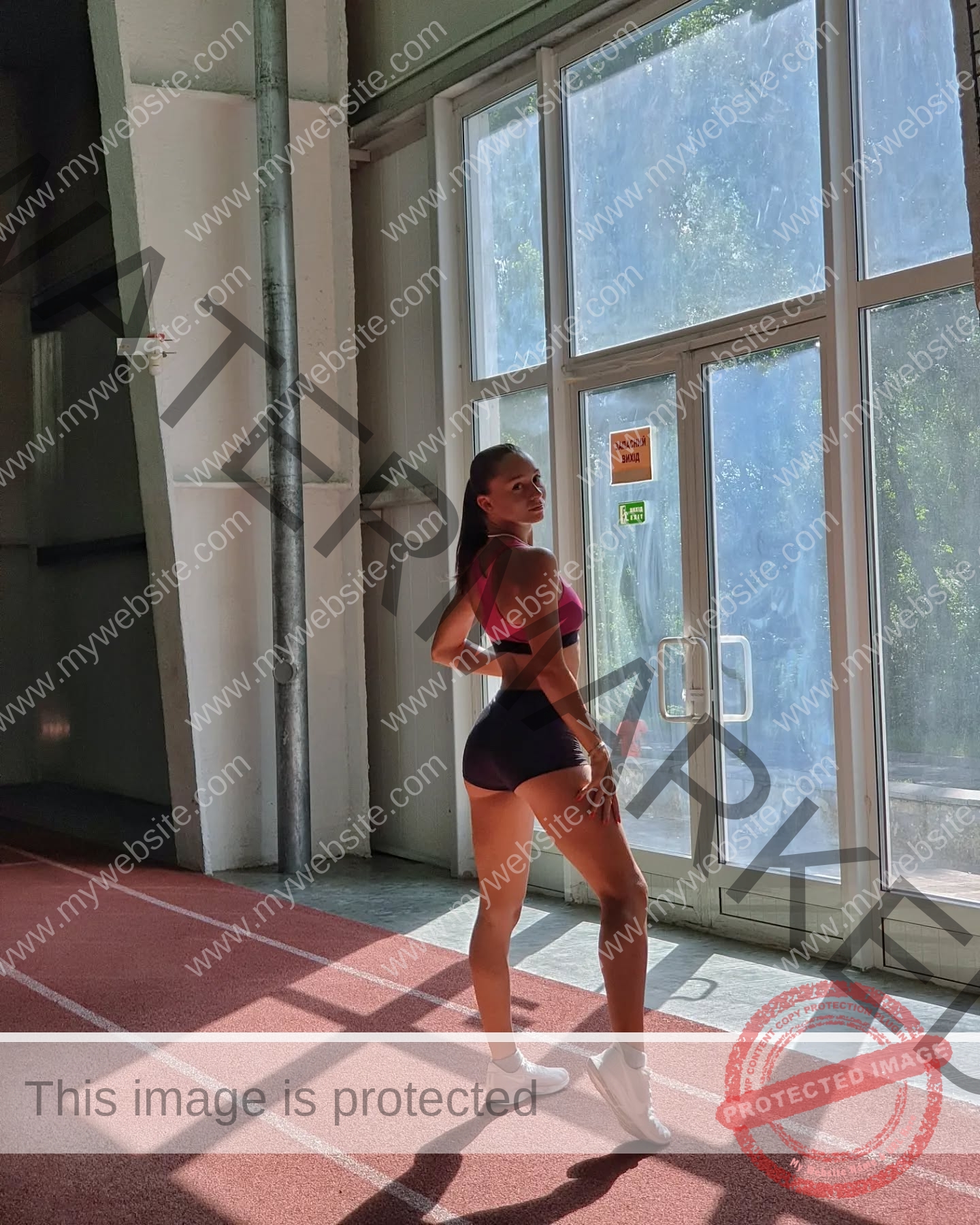 diana-honcharenka-ukraine-goncharenko_43-09636 Diana Honcharenka, track athlete from Ukraine, stands in athletic wear on an indoor track, sunlight streaming in, posing confidently.