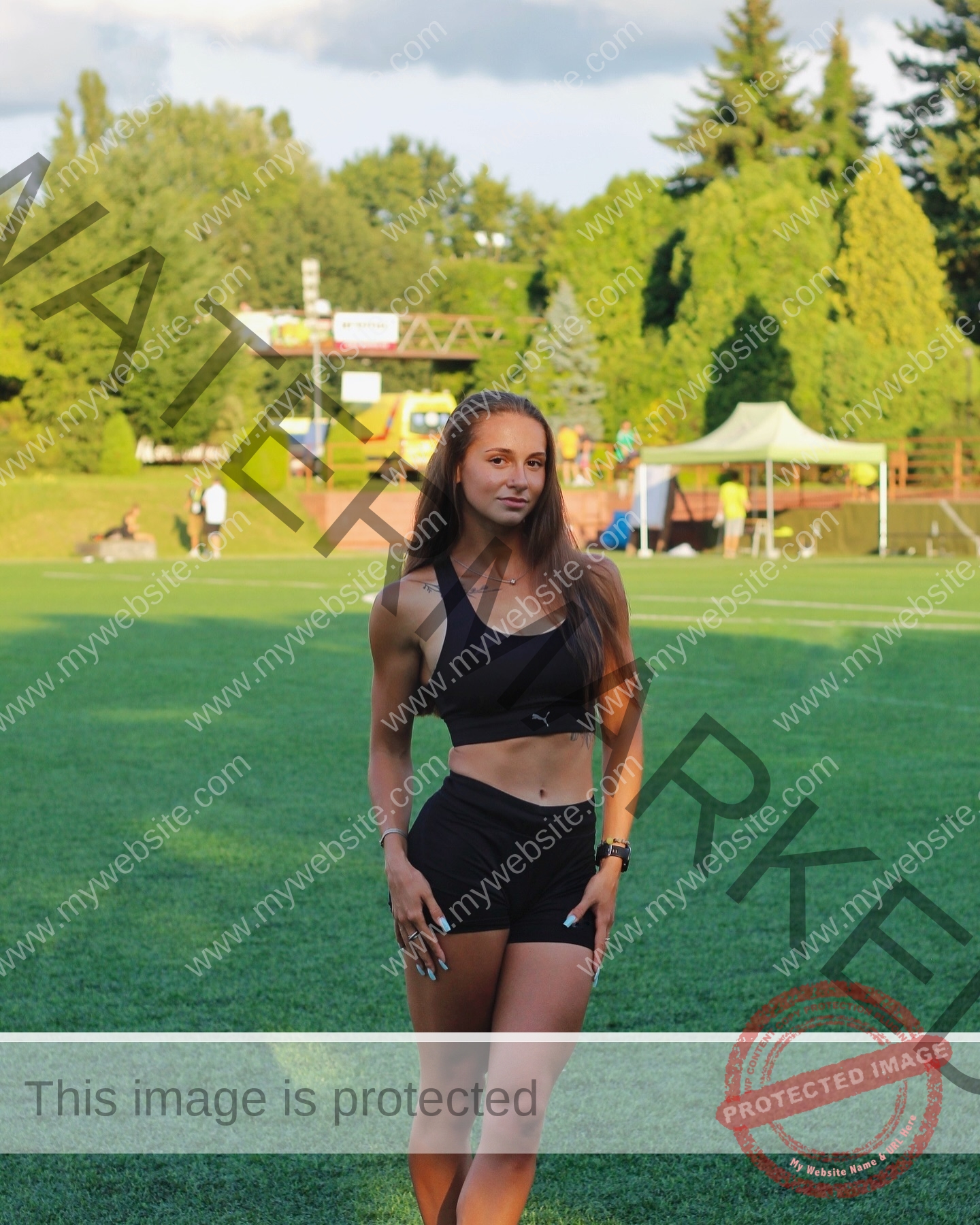 diana-honcharenka-ukraine-goncharenko_43-09833 Diana Honcharenka, track athlete from Ukraine, in black athletic wear stands on a field with trees and tents behind her under clouds.