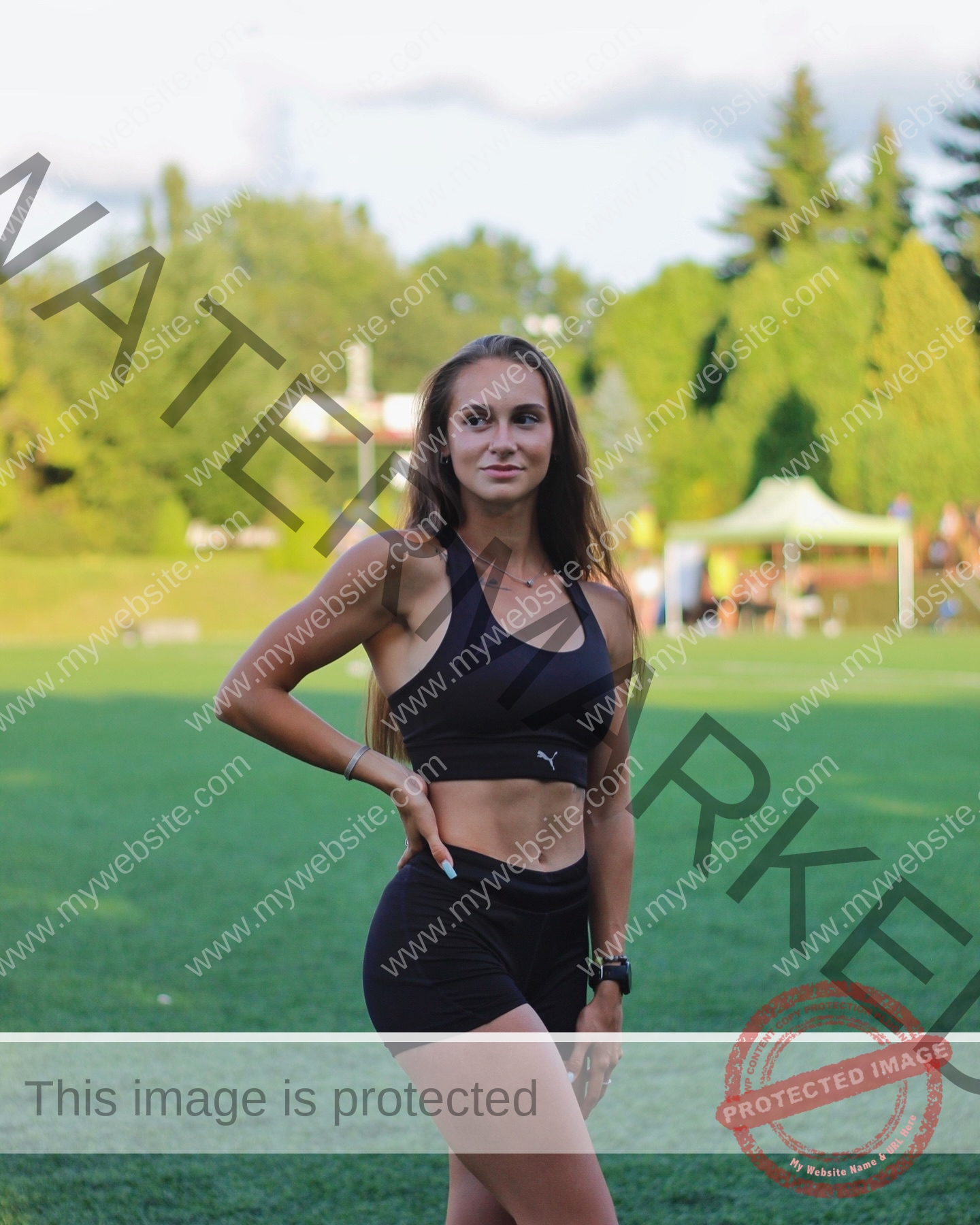 diana-honcharenka-ukraine-goncharenko_43-09834 Diana Honcharenka, track athlete from Ukraine, in black athletic wear poses on a grassy field with trees and tents behind her.