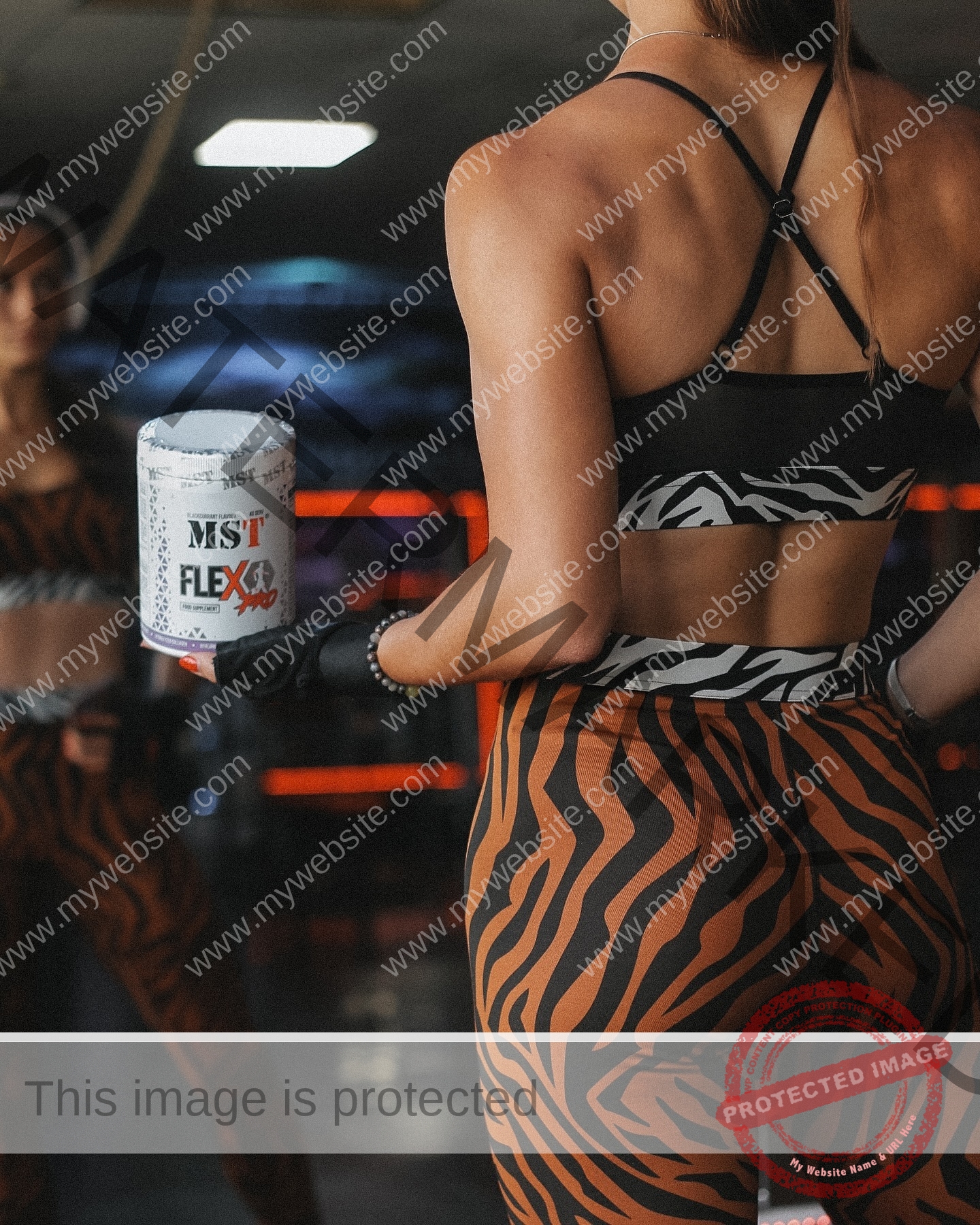 diana-honcharenka-ukraine-goncharenko_43-09848 Diana Honcharenka, track athlete from Ukraine, wears zebra and tiger-print activewear, holding MST FLEX in a gym with mirrored walls.