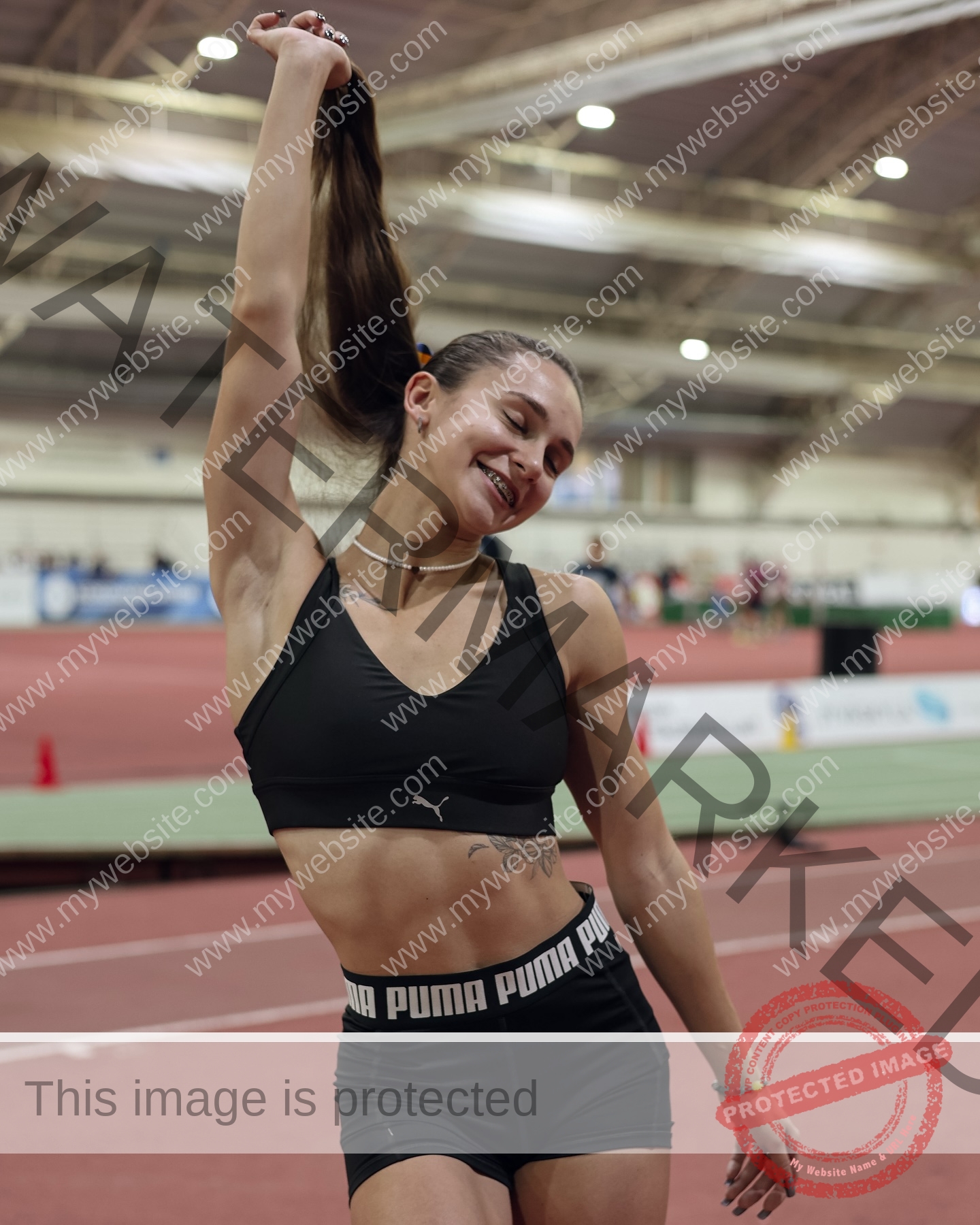 diana-honcharenka-ukraine-goncharenko_43-09870 Diana Honcharenka, track athlete from Ukraine, smiles and raises her ponytail on an indoor track, looking happy and relaxed.