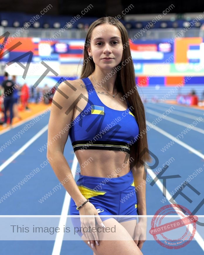 Diana Honcharenka, track athlete from Ukraine, stands on an indoor track in a blue and yellow uniform, looking at the camera.