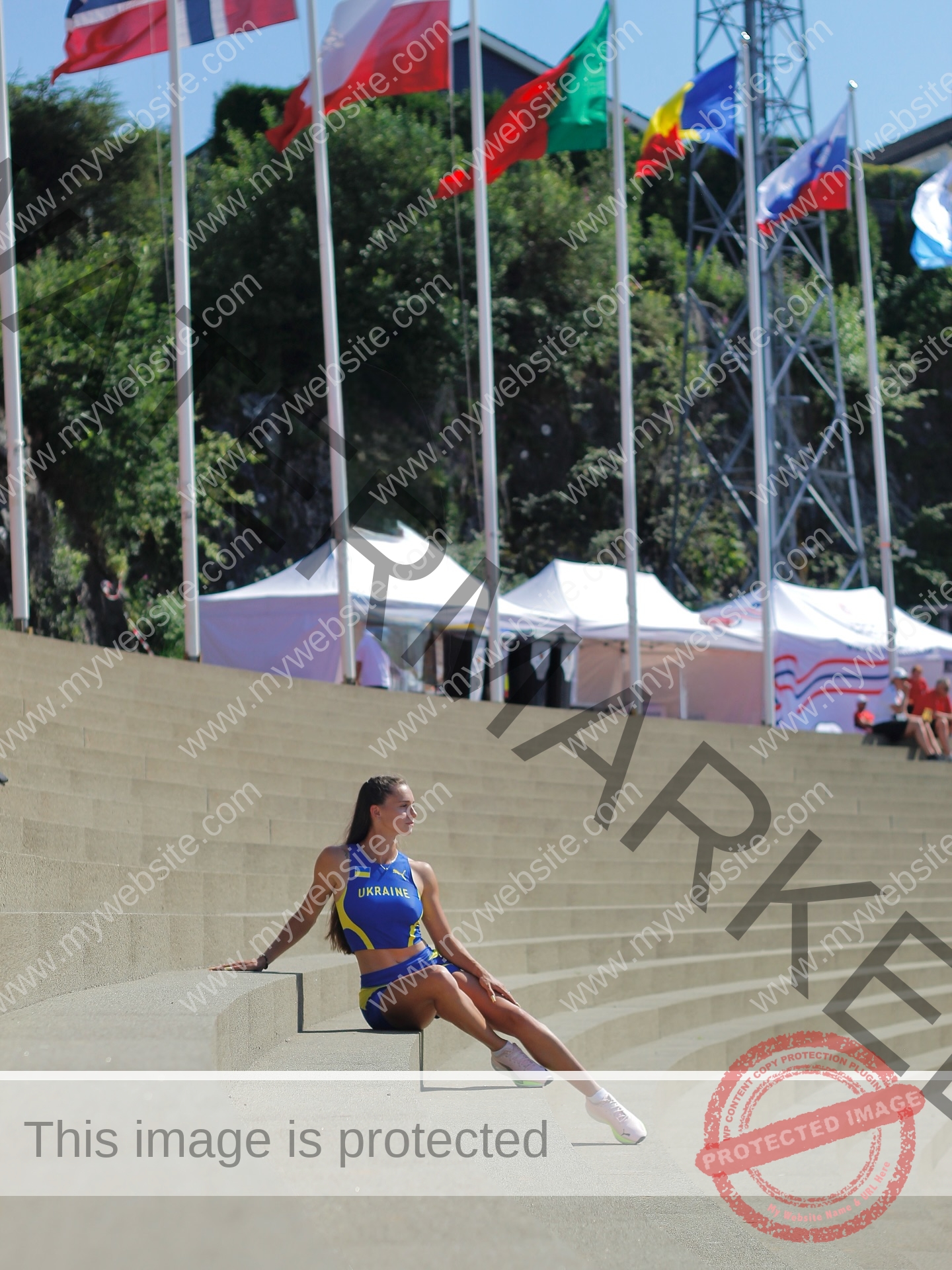 diana-honcharenka-ukraine-goncharenko_43-09929 Diana Honcharenka, track athlete from Ukraine, sits on stadium steps in blue and yellow, with flags and tents on a sunny day.