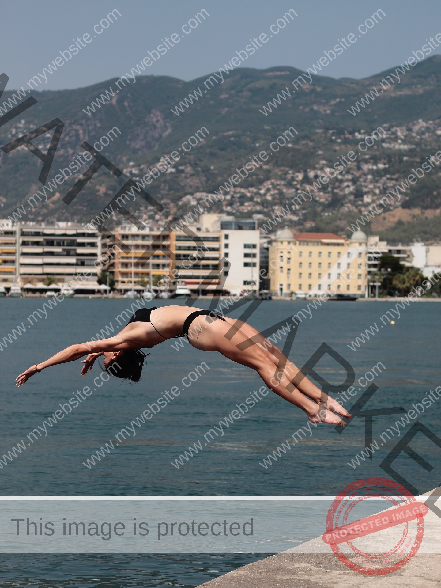 diana-honcharenka-ukraine-goncharenko_43-09938 Diana Honcharenka, track athlete from Ukraine, in a black bikini dives off a concrete edge into water, city and mountains behind.