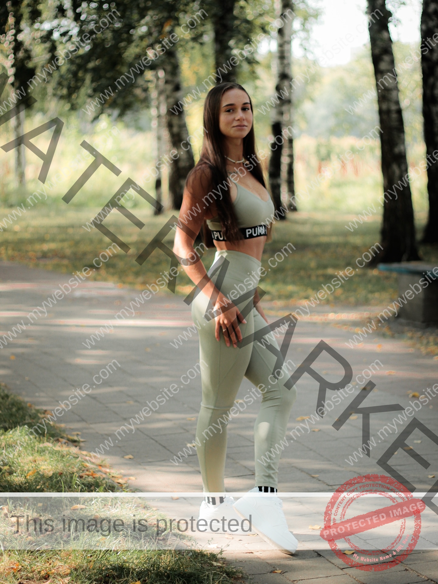 diana-honcharenka-ukraine-goncharenko_43-09950 Diana Honcharenka, track athlete from Ukraine, in light green athletic wear and white sneakers stands on a paved park path, looking at the camera.