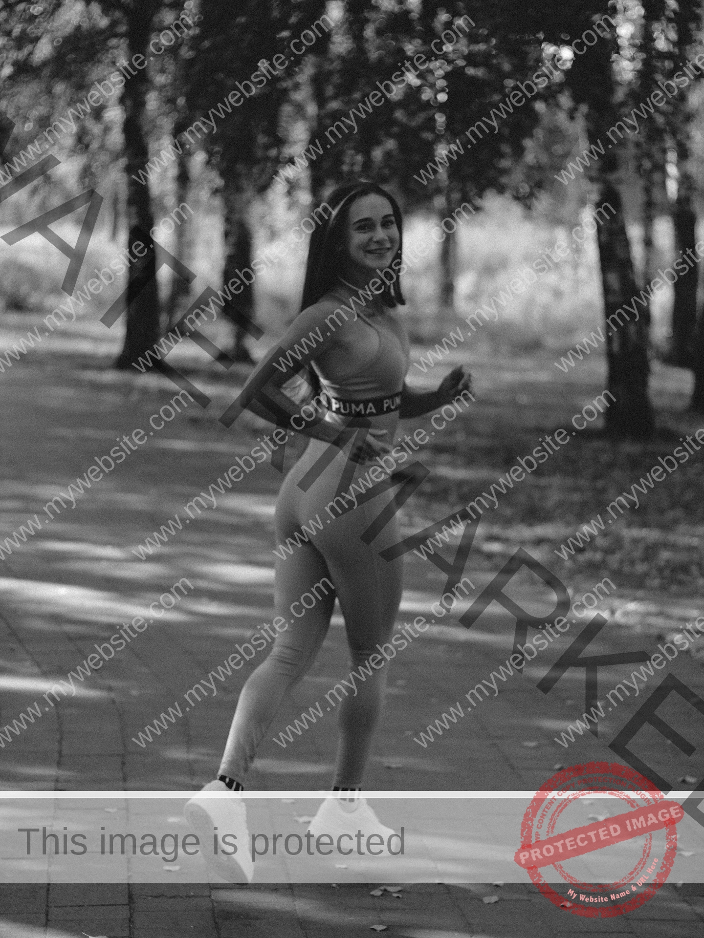 diana-honcharenka-ukraine-goncharenko_43-09952 Diana Honcharenka, track athlete from Ukraine, jogs in athletic wear along a tree-lined park path in a black and white photo.