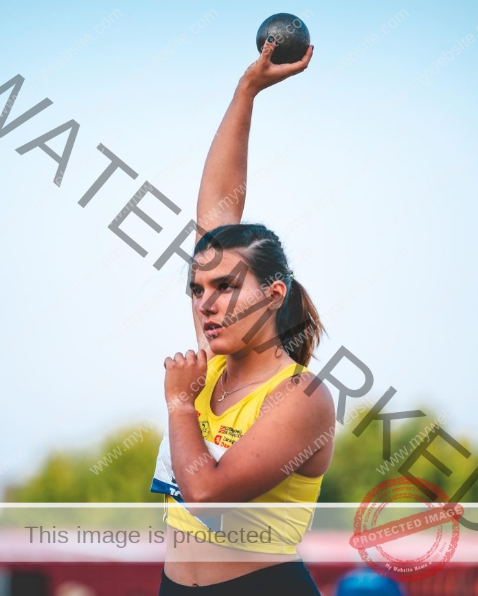 Eva Luna Lozano, javelin thrower from Spain, a female athlete in yellow prepares to throw a shot put outdoors with trees behind.