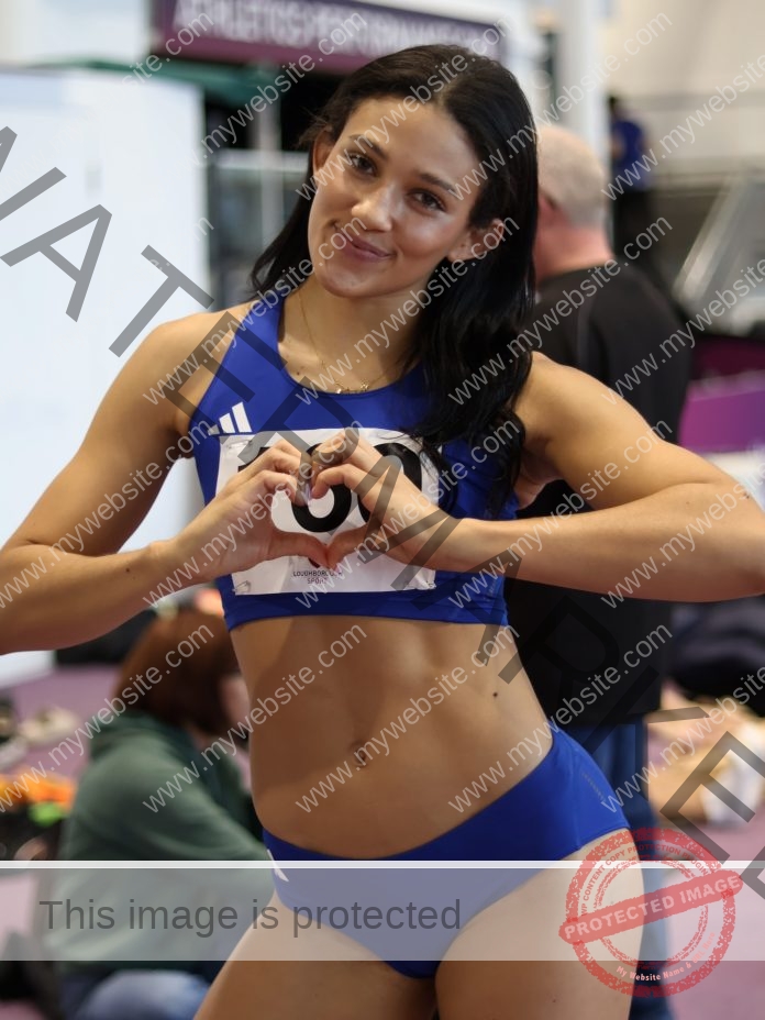 Georgie Forde Wells Georgie Forde Wells, an English track athlete, stands indoors in blue sportswear, smiling and making a heart shape.