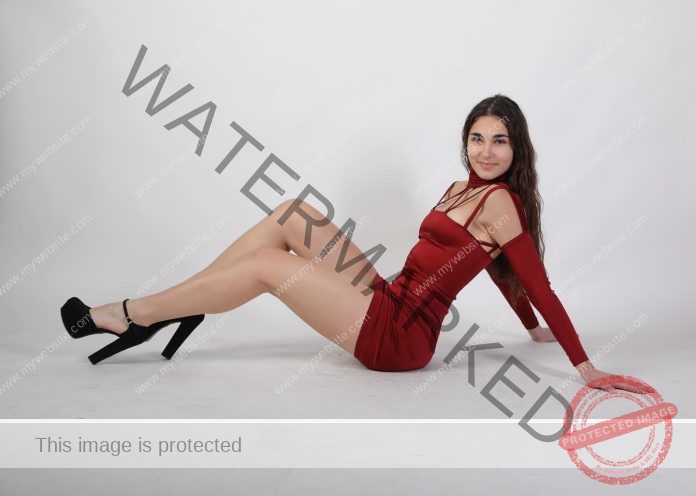 Minafra Giulia Minafra, a woman with long brown hair, sits on the floor in a red dress and black heels, smiling softly at the camera.