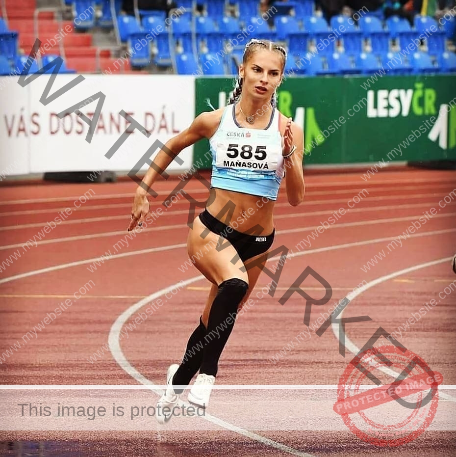 karolina-manasova-czechia-karolina_manasova-318 Karolina Manasova A female track and field athlete in black shorts, white crop top, black knee-high socks sprints 100m on wet Czech track.