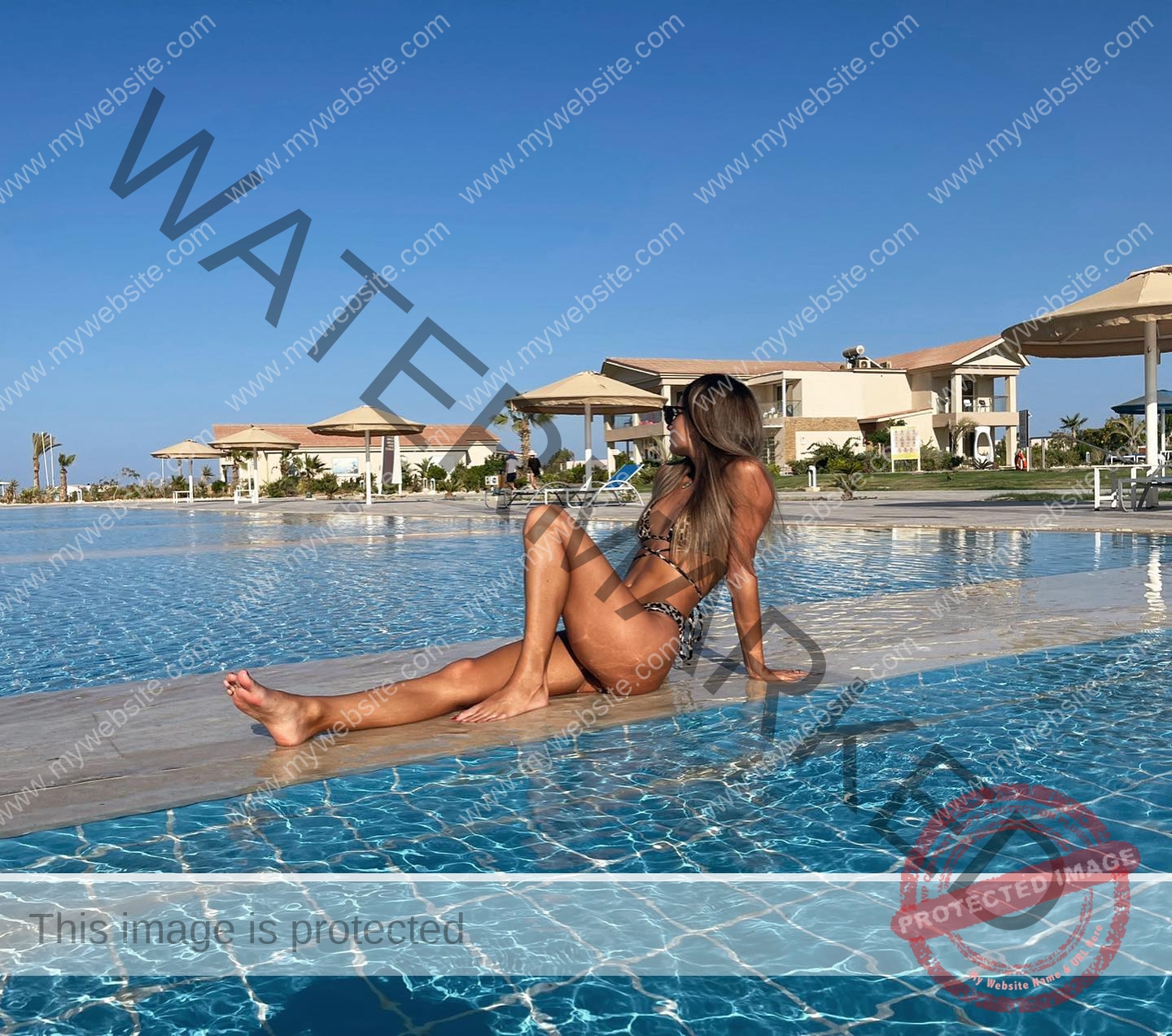 karolina-manasova-czechia-karolina_manasova-322 Karolina Manasova Karolina Manasova relaxes in a bikini by a blue pool, facing away; resort buildings, chairs, and umbrellas nearby.