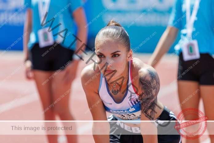 Karolina Manasova Karolina Manasova, a Czech track athlete with a left arm tattoo, leans at the 100m start as staff in blue look on.