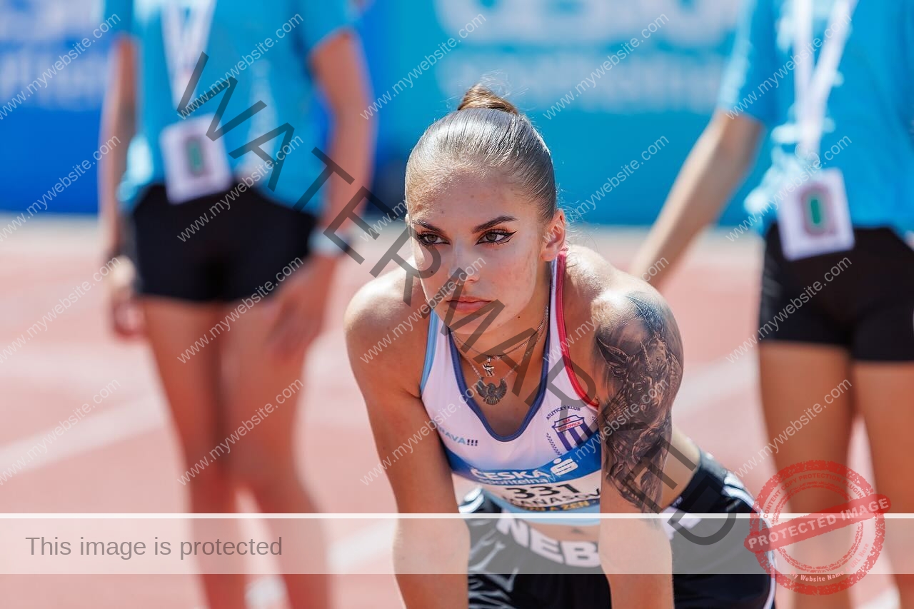 karolina-manasova-czechia-karolina_manasova-357 Karolina Manasova Karolina Manasova, a Czech track athlete with a left arm tattoo, leans at the 100m start as staff in blue look on.
