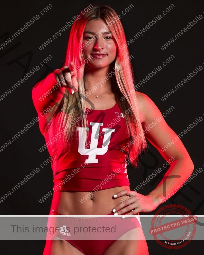 Kylee Poulton A track and field athlete, Kylee Poulton, stands confidently in a red Indiana University uniform, smiling and pointing at the camera with dramatic red lighting against a black background.