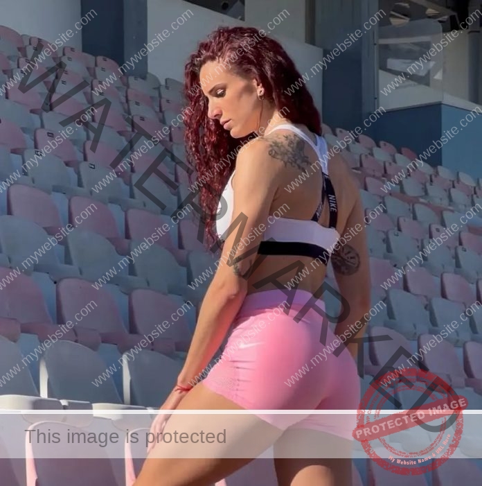 Laura Bueno Track and field athlete Laura Bueno of Spain, long curly hair, in a white sports bra and pink shorts stands in a stadium.