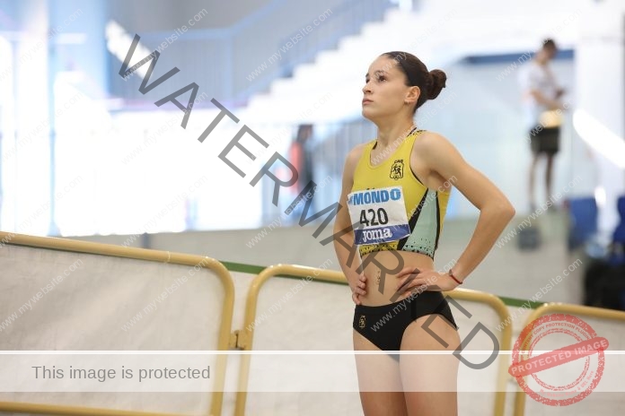 Laura Castillo, a female track and field athlete from Spain in a yellow and black kit numbered 420, stands hands on hips, focused indoors.
