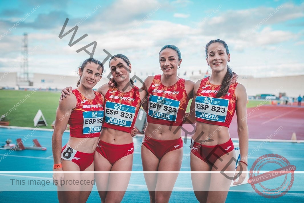 laura-castillo-spain-laura_c.i_-3266 Laura Castillo Four female track and field athletes from Spain, including Laura Castillo, smile in red uniforms on a blue track outdoors.