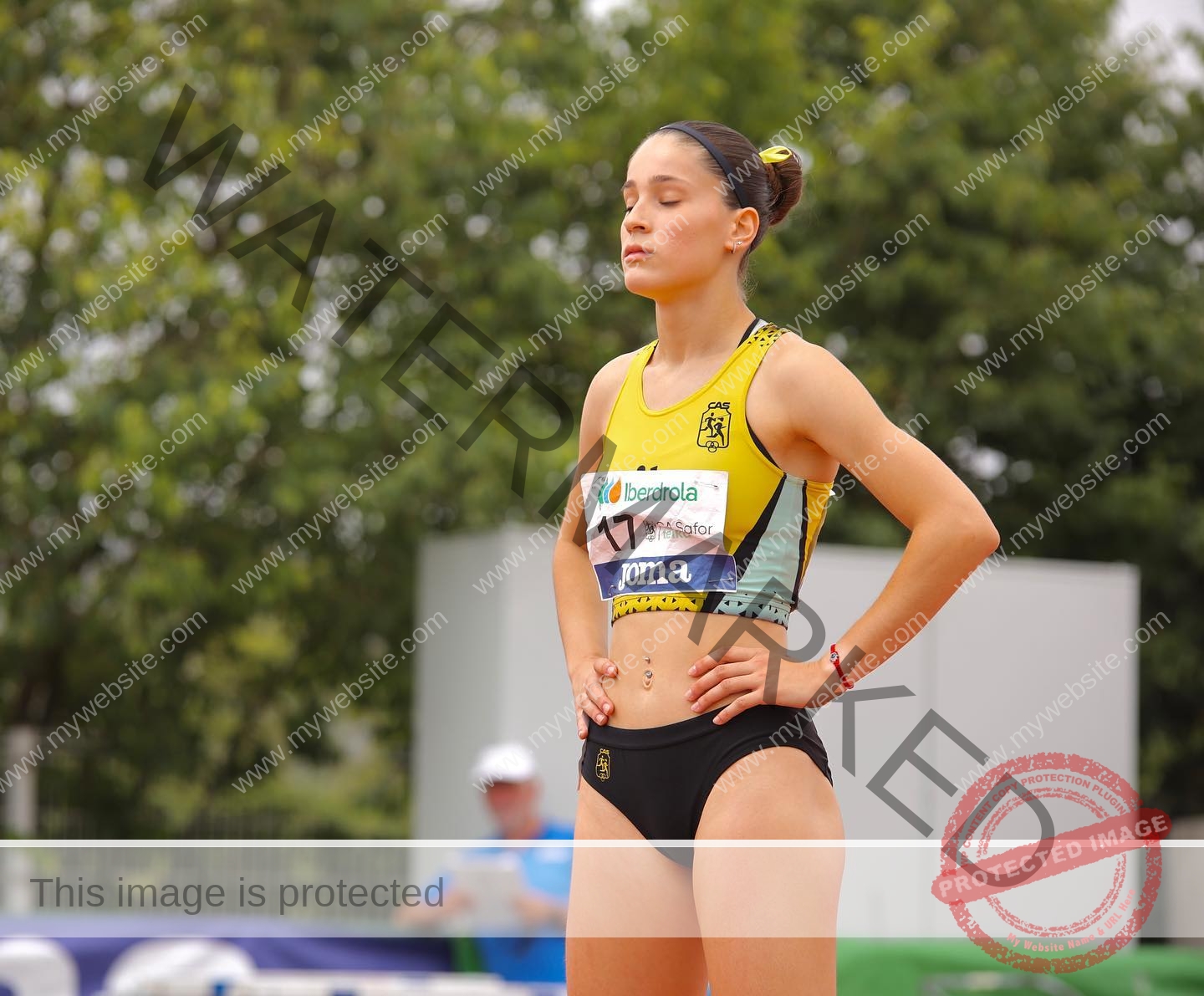laura-castillo-spain-laura_c.i_-3270 Laura Castillo, a female track and field athlete from Spain, stands hands on hips, eyes closed in yellow and black uniform outdoors.