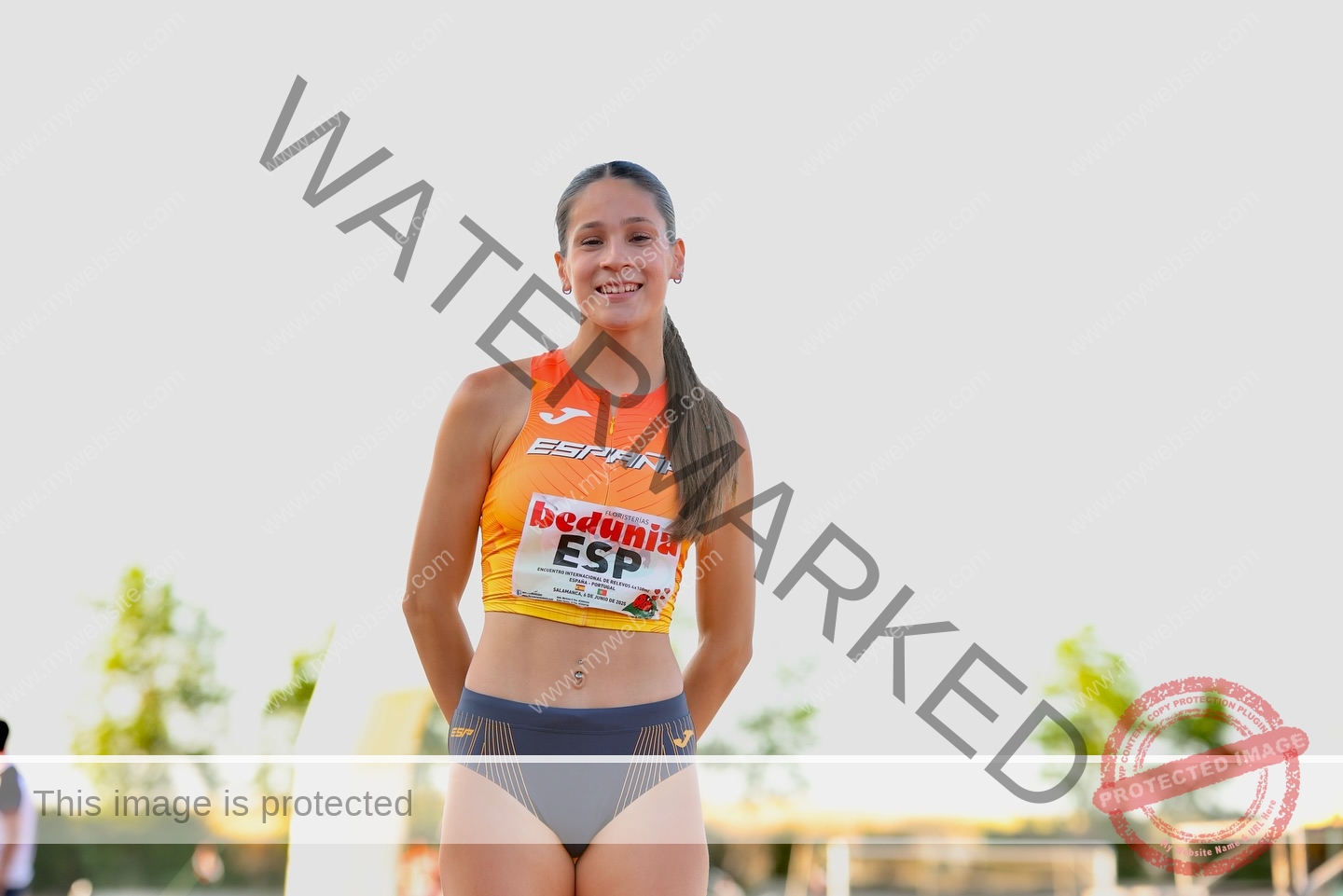 laura-castillo-spain-laura_c.i_-3291 Laura Castillo, a female track and field athlete in orange and gray, smiles outdoors with an ESP bib; blurred sky and trees behind.