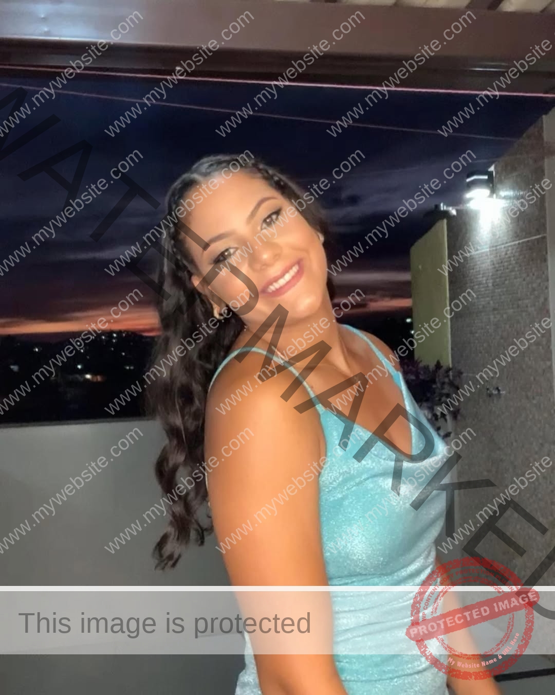 maria-eduarda-dantas-brazil_dudinha_23-1641 Maria Eduarda Dantas, discus thrower from Brazil, smiles at the camera in a shiny blue top with city lights and sunset behind her.