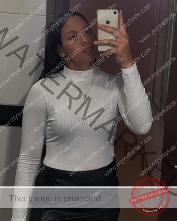 Maria Eduarda Dantas, discus thrower from Brazil, wears a white turtleneck and black skirt, taking a mirror selfie with her phone.