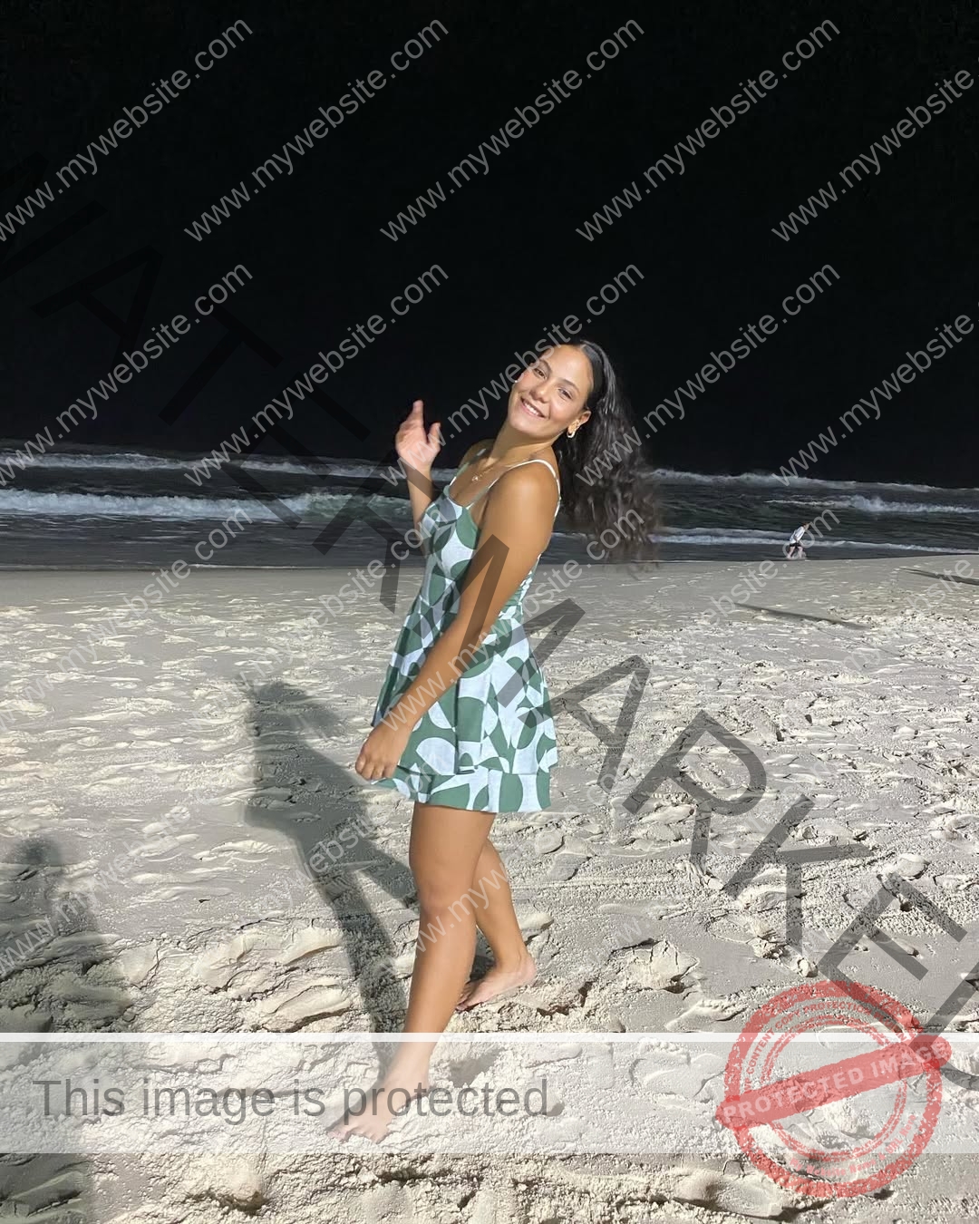 maria-eduarda-dantas-brazil_dudinha_23-1649 Maria Eduarda Dantas, discus thrower from Brazil, smiles barefoot in a patterned dress on a sandy beach at night, waves behind her.