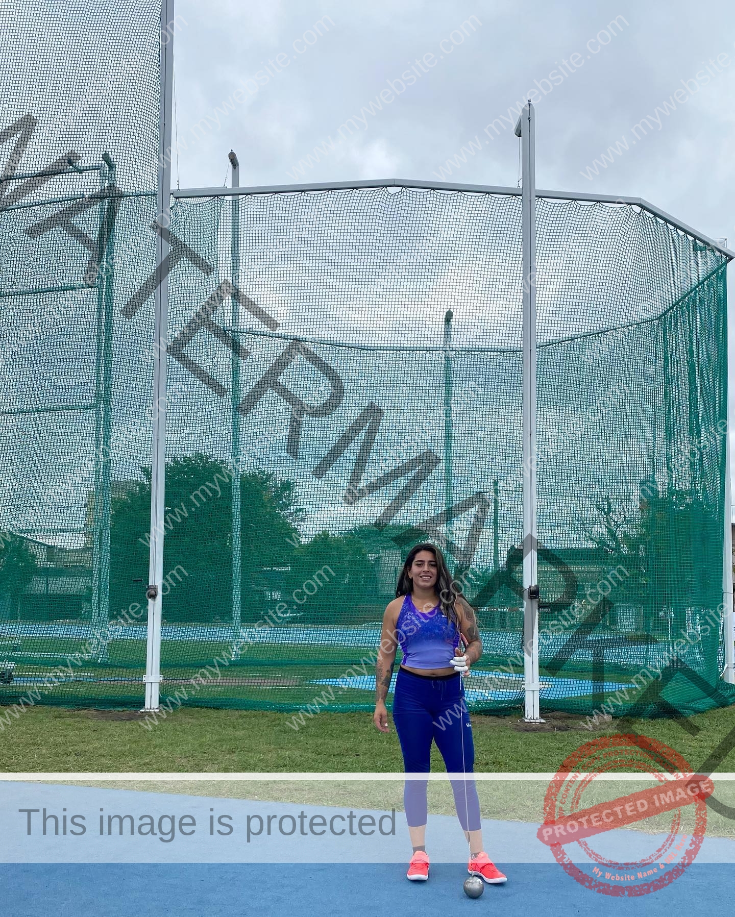 mariana walker-childe-marianawalker_-1687 Mariana Walker, hammer thrower from Chile, wears a purple top, blue leggings, red shoes on a blue track with a hammer ball.