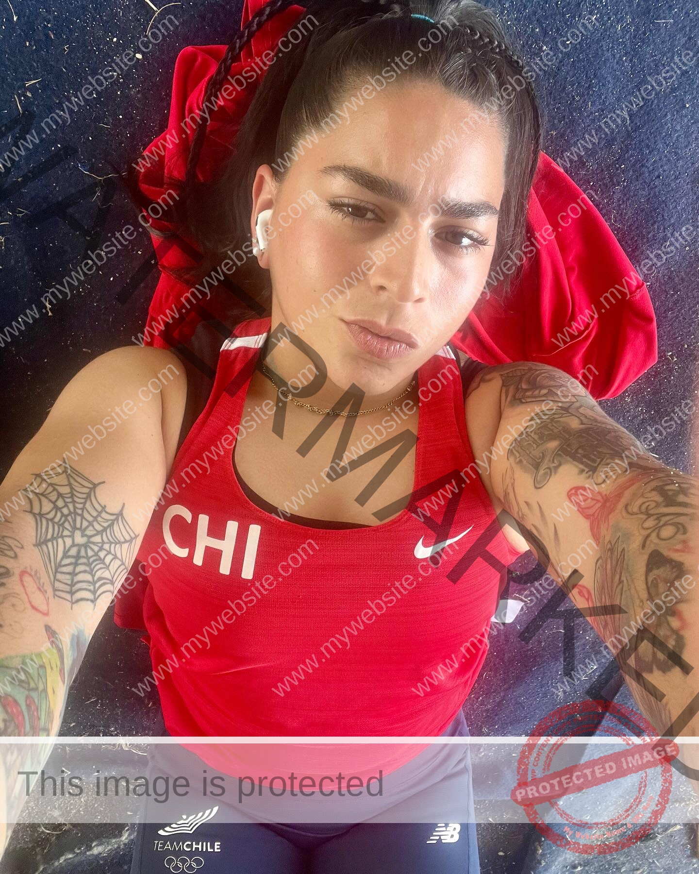 mariana walker-childe-marianawalker_-1855 Mariana Walker, hammer thrower from Chile, with tattoos, in a CHI tank and Team Chile shorts, takes a selfie lying on the ground.