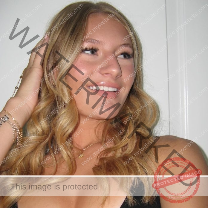 Mckenna Panos A young woman with wavy blonde hair smiles while looking to the side, wearing a black top and gold jewelry.
